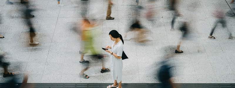 Imagem de uma mulher utilizando seu smartphone em uma calçada movimentada