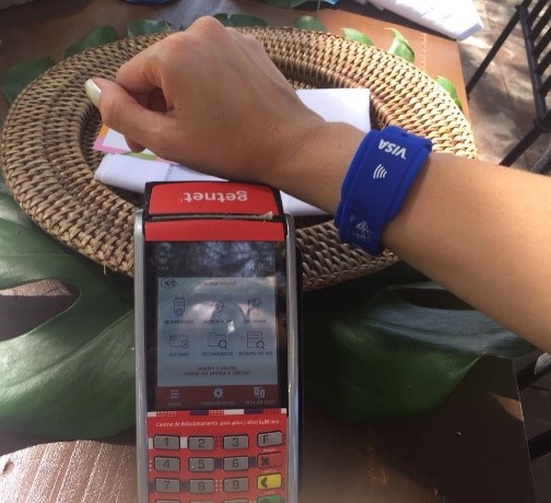 Mão feminina realizando um pagamento por aproximação com uma pulseira da Visa