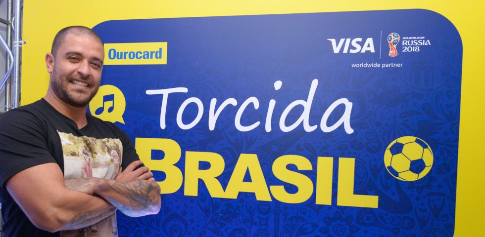 Diogo Nogueira sorrindo ao lado do banner da Torcida Brasil