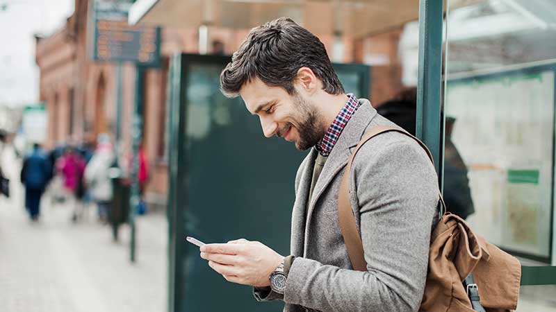 Homem sorrindo enquanto usa seu smartphone na rua