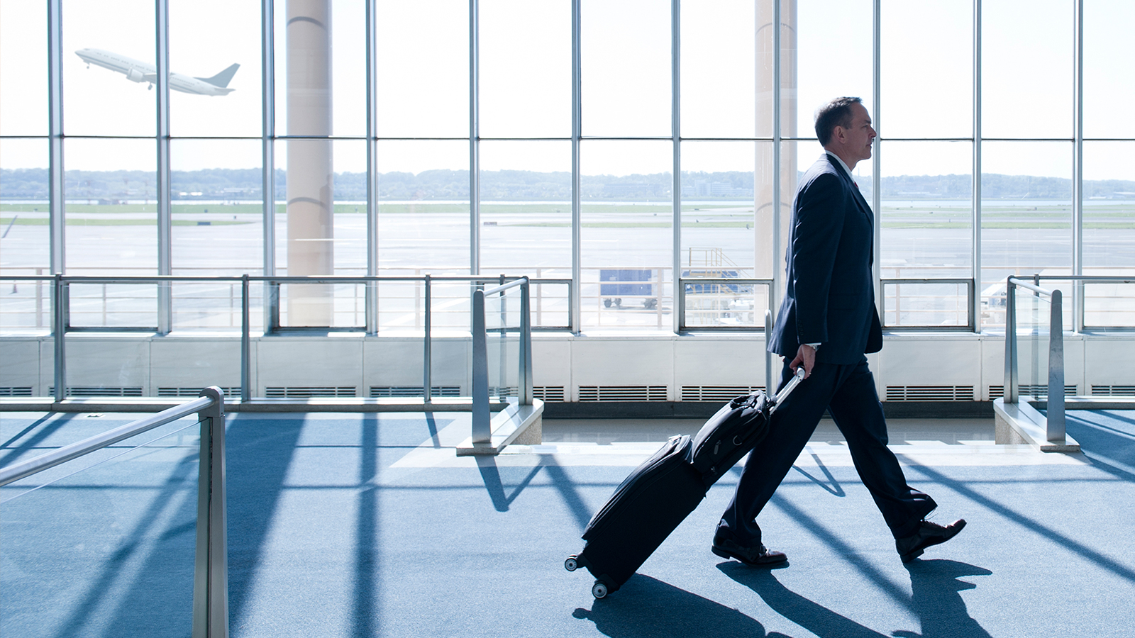 Business man with rolling suitcase walking in airport terminal.