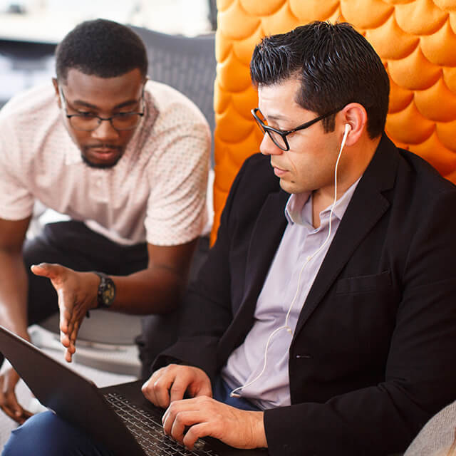 Two men collaborating with one man typing on his laptop.