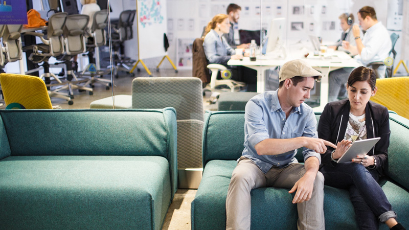 Man and woman working together on a tablet in a friendly, collaborative environment.
