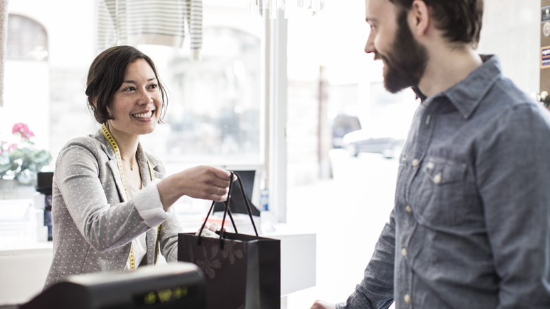 Woman shopping on a smart phone Female design professional giving a shopping bag to customer at cash counter in a studio space.