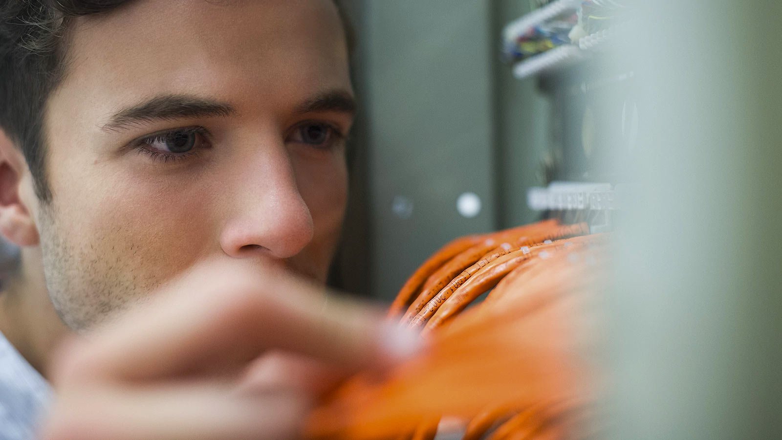 Close up of a man investigating wires in a server room.