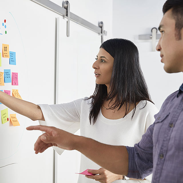 Two workers collaborating on a whiteboard covered with Post-its.