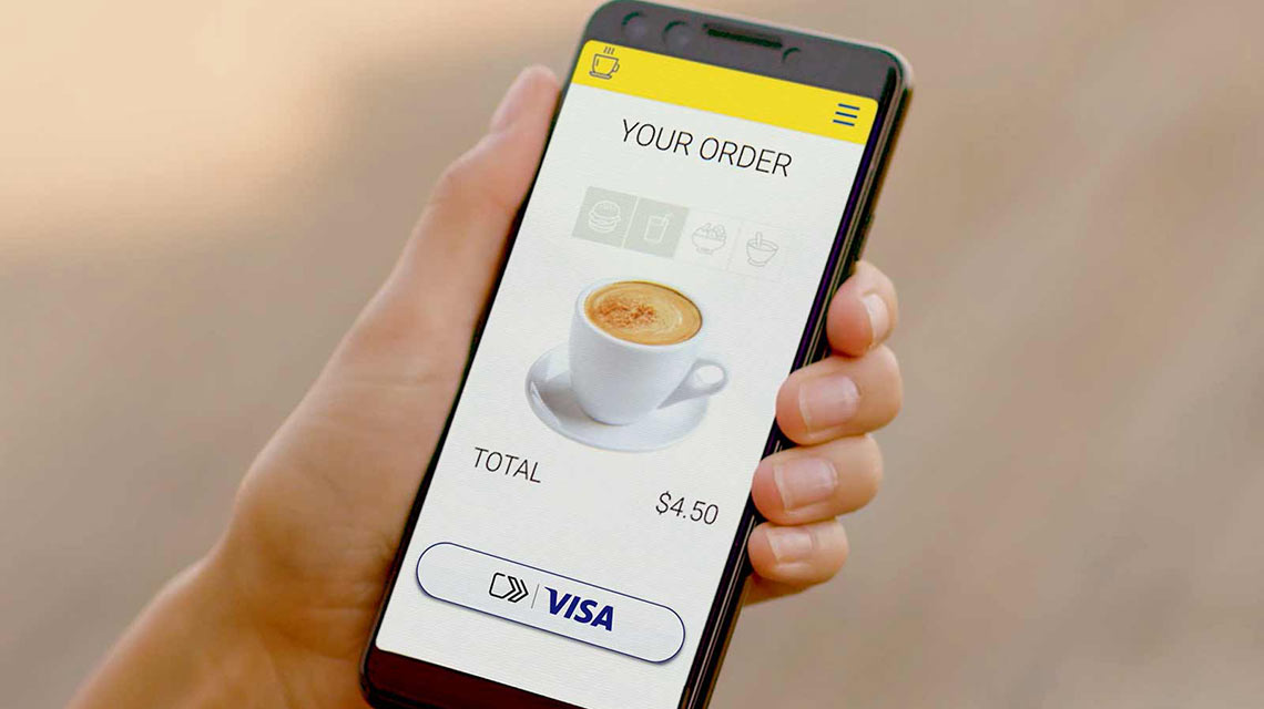 Person holding cellphone and ordering a cup of coffee using Visa Checkout service.