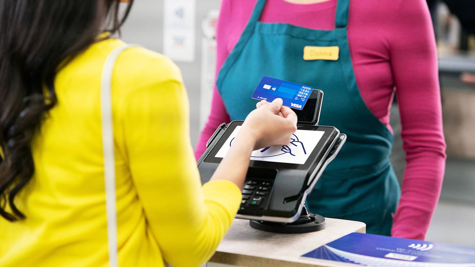 Woman making a contactless payment at a payment terminal while the merchant stands in front of her.