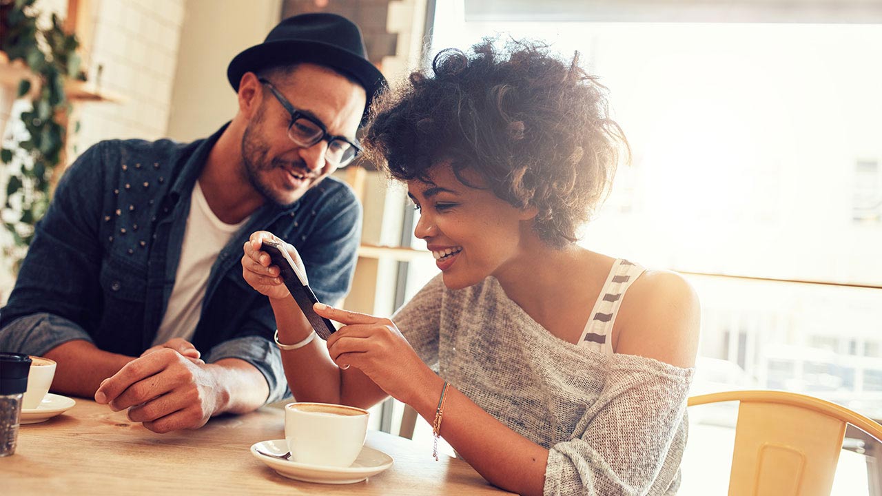 Smiling couple seated at table in café looking at mobile phone.