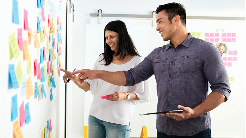 Idea board covered in post-its being discussed by man and woman.