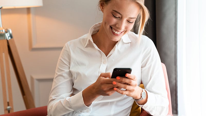 Mulher usando celular e sorrindo.