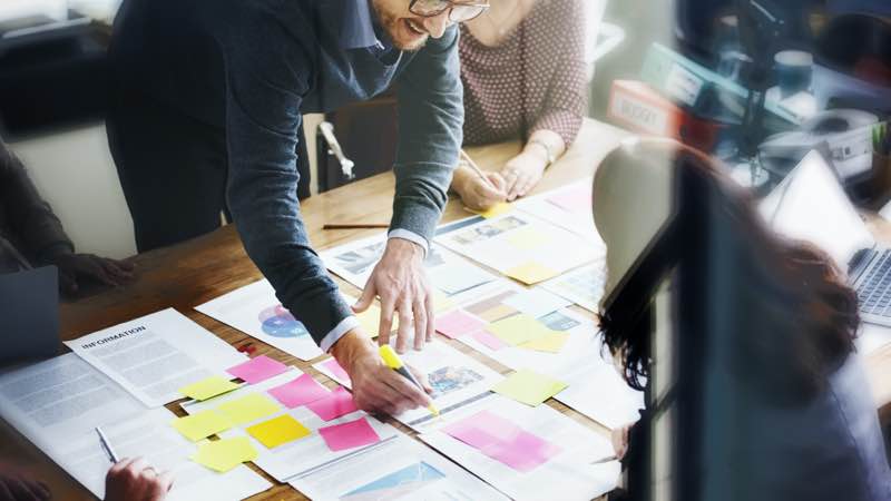 Pessoas debruçadas sobre uma mesa com vários papéis e post-its