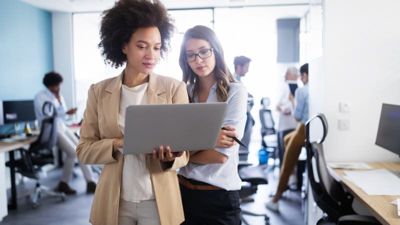 Duas mulheres de perfil corporativo analisando tela do notebook