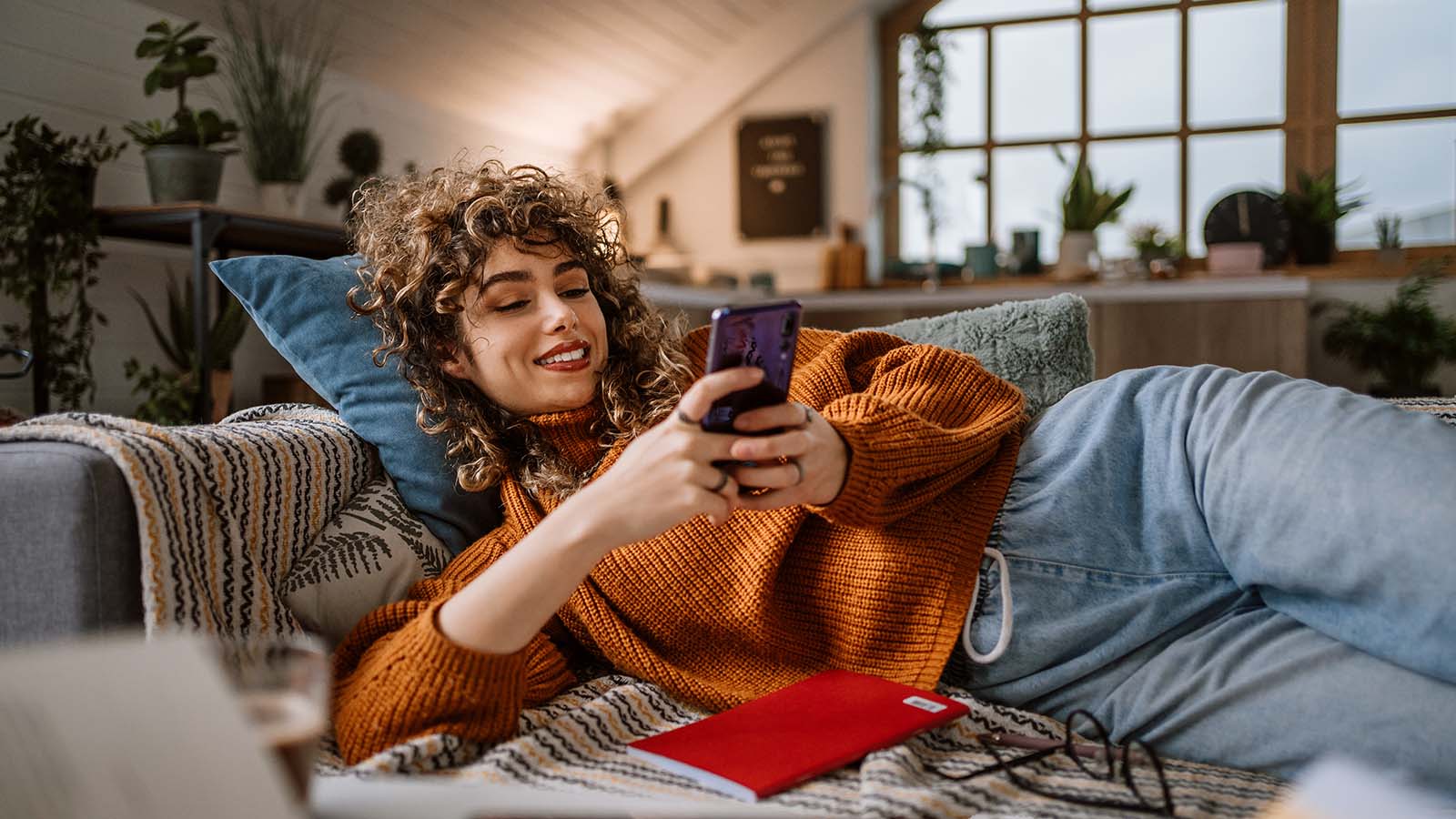 Imagem exibe jovem moça sorridente utilizando seu smartphone.