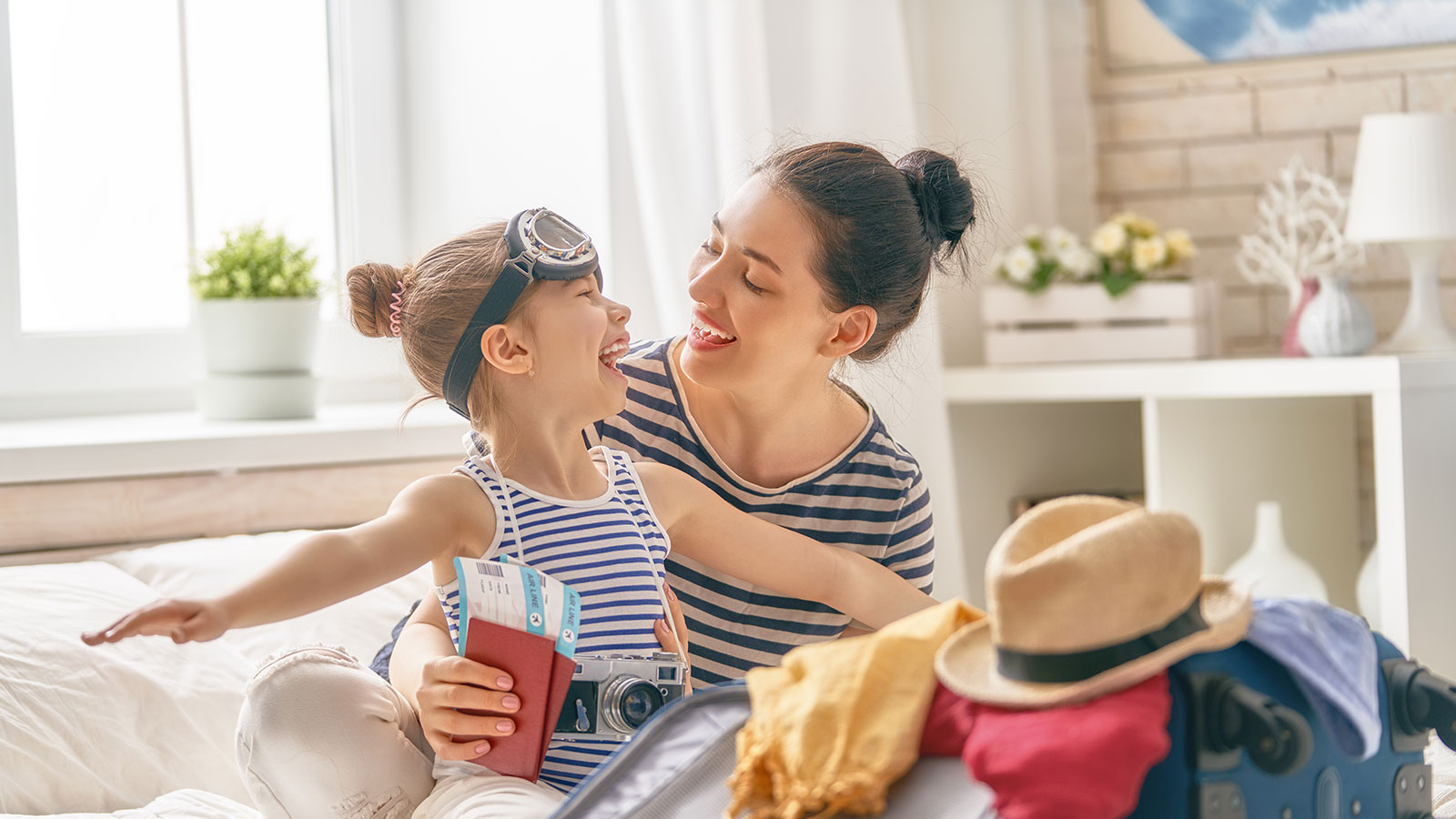 Mãe e filha sorrindo e fazendo as malas com passagens de viagem na mão