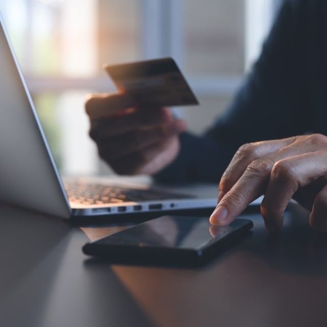 Pessoa com cartão e smartphone em frente ao notebook