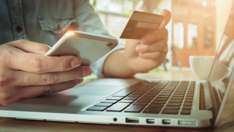 Pessoa com smartphone e cartão em mãos em frente ao notebook