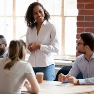 Equipe reunida com uma mulher de pé conduzindo a reunião