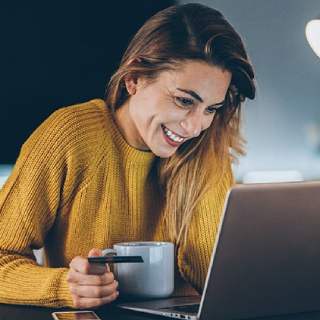 Mulher sorri para o notebook com uma caneca na mão