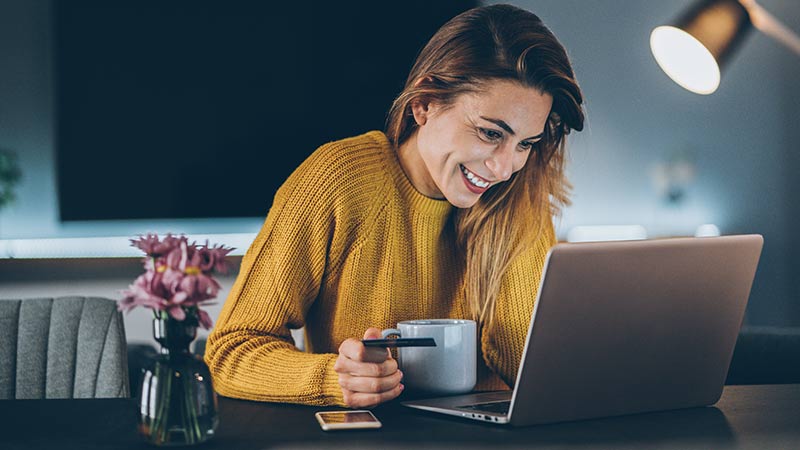 Mulher sorri para o notebook com uma caneca na mão