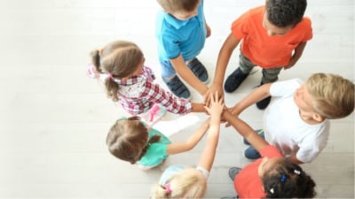Grupo de crianças em círculo juntando as mãos no centro