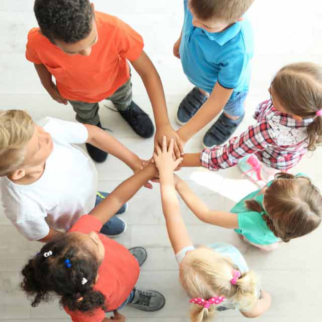 Grupo de crianças em círculo juntando as mãos no centro