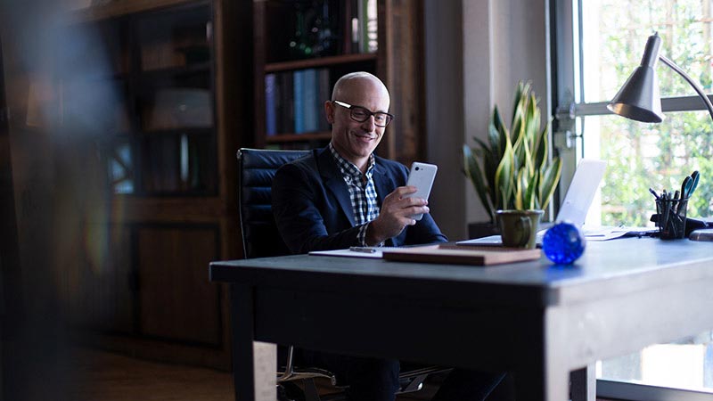 Homem de perfil corporativo observando o celular um escritório sofisticado