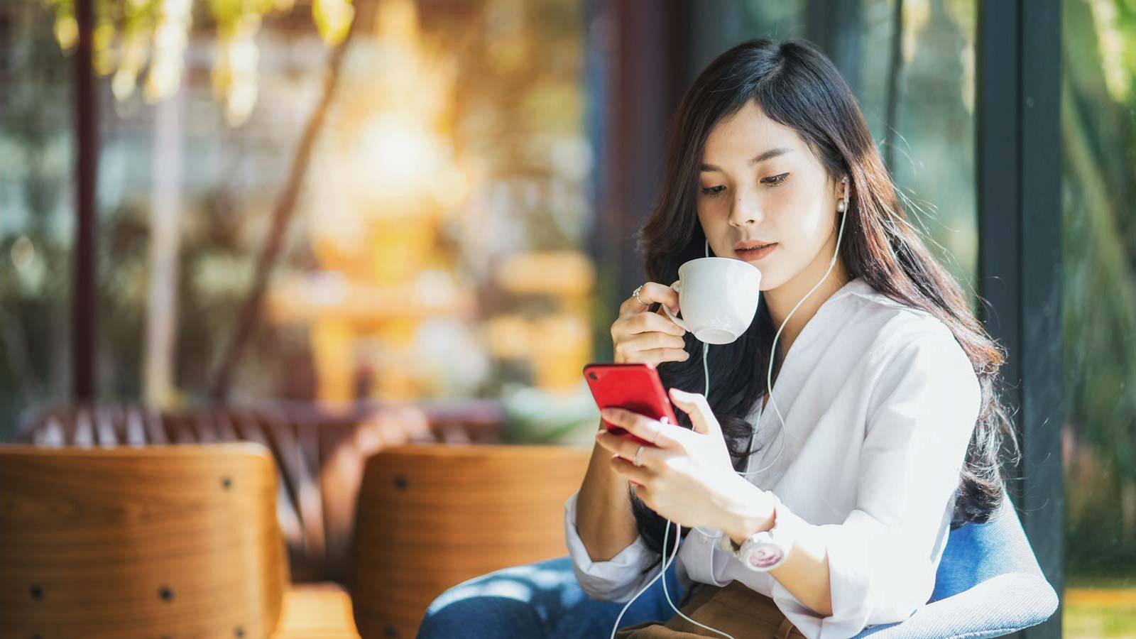 Mulher com fone de ouvido assistindo algo no celular enquanto toma café