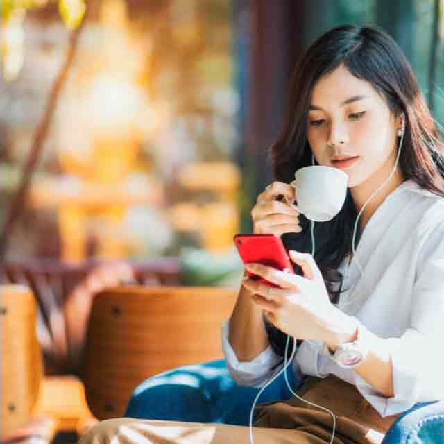 Mulher tomando café e olhando o celular.