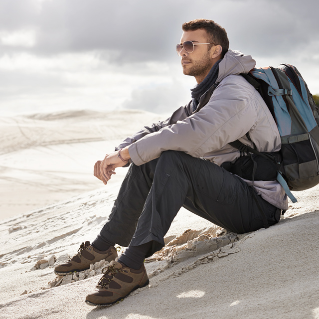 Homem com mochila sentado em dunas de areia