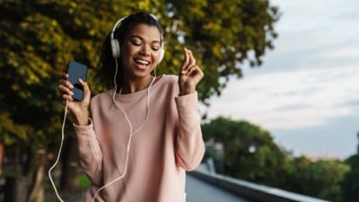 Imagem exibe mulher usando fone de ouvidos, segurando celular e estralando os dedos