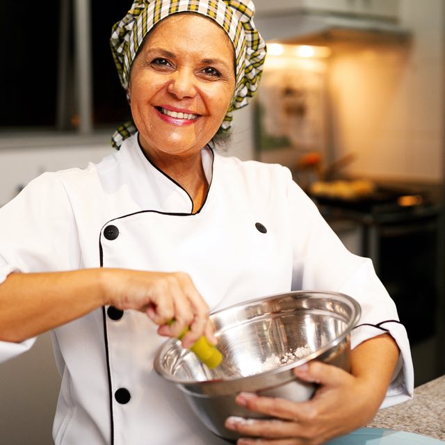 Mulher com uniforme de chef batendo algo numa vasilha de alumínio