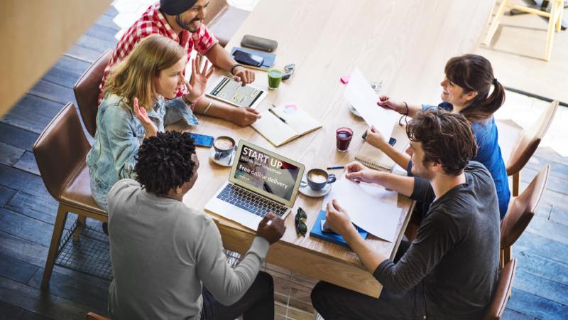 Equipe de trabalho se reúne com cadernos e notebook para conversar