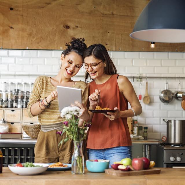 Duas mulheres sorrindo e olhando o seu iPad numa cozinha espaçosa