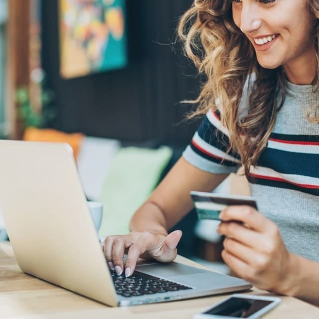 Mulher segurando cartão e comprando online com seu notebook