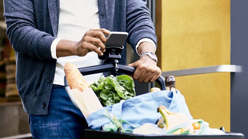 Imagem de uma pessoa empurrando um carrinho de compras e utilizando seu smartphone