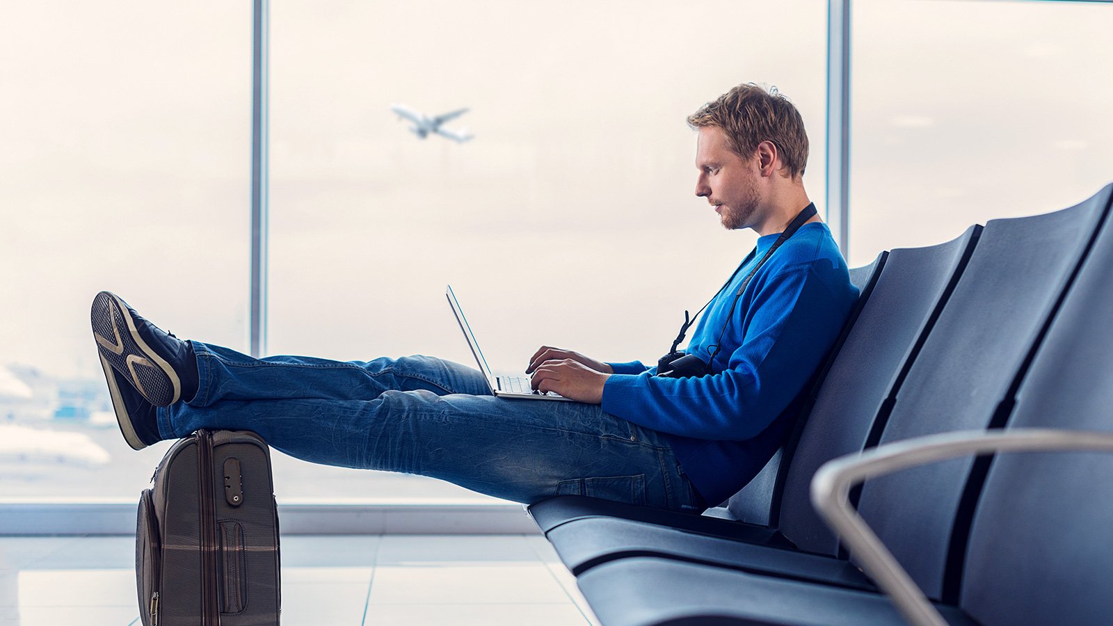 Homem sentado no aeroporto com notebook e bagagem