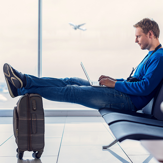 Homem sentado no aeroporto com notebook e bagagem