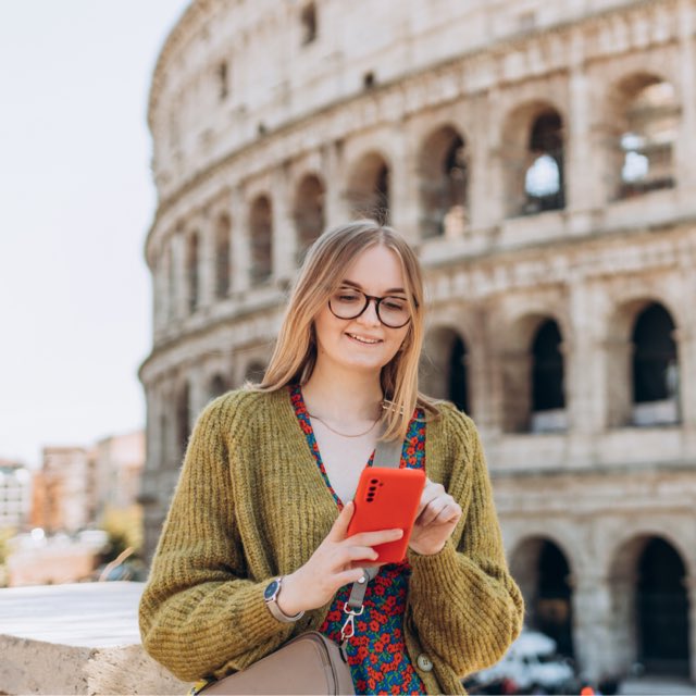 Imagem exibe mulher mexendo no celular em frente ao Coliseu