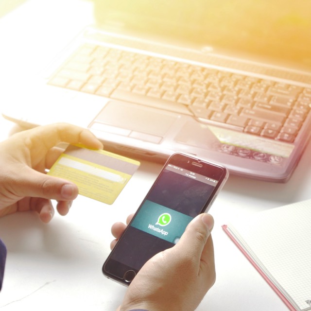 Imagem de uma pessoa segurando um cartão de crédito e um smartphone com o aplicativo Whatsapp aberto