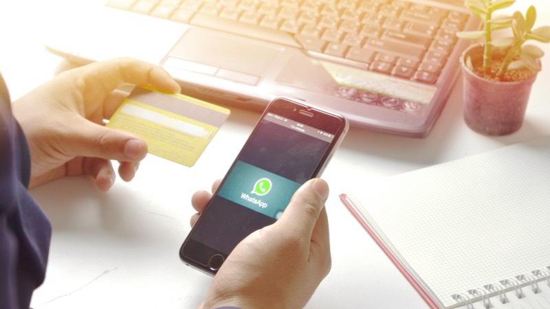 Imagem de uma pessoa segurando um cartão de crédito e um smartphone com o aplicativo Whatsapp aberto