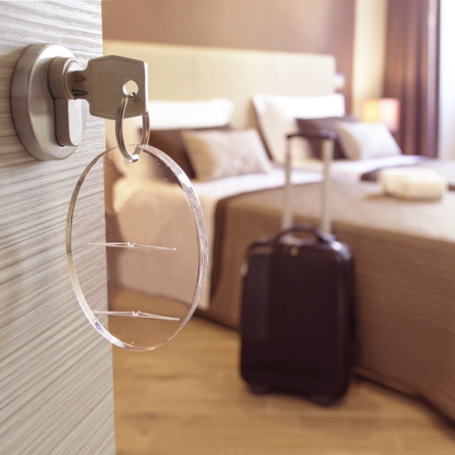 Imagem de um quarto de hotel com a porta aberta e uma mala ao lado da cama