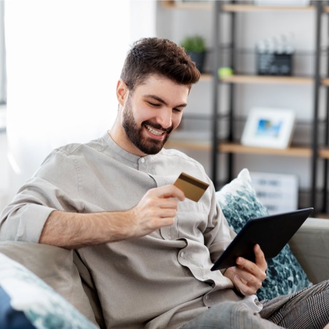 Imagem exibe homem sorridente segurando cartão de débito e tablet. 