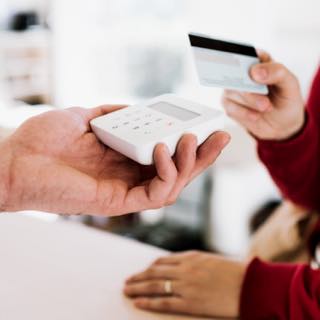 Imagem de uma pessoa segurando uma máquina de cartão e outra com um cartão realizando pagamento