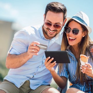 Casal sorrindo pagando online com seu cartão de crédito e tablet na rua