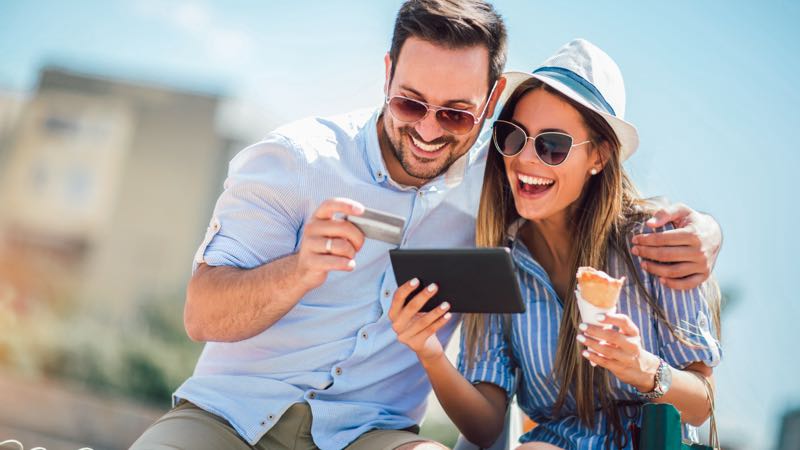 Casal sorrindo pagando online com seu cartão de crédito e tablet na rua