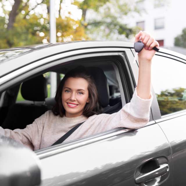 Mulher, dentro do carro, sorrindo e segurando a chave do carro