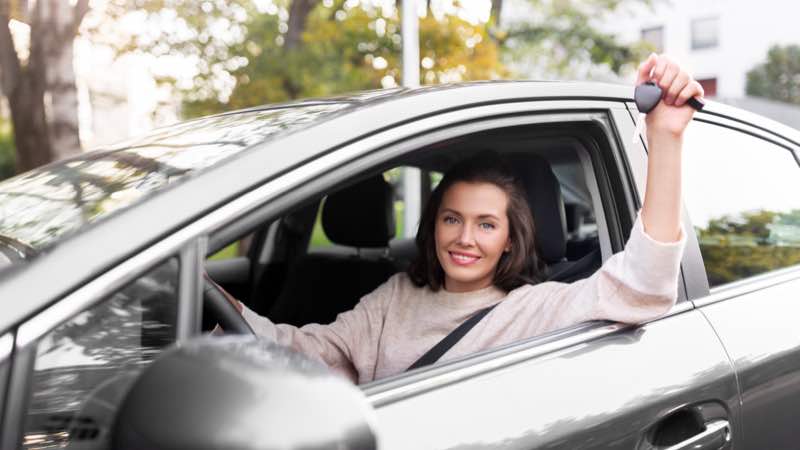 Mulher, dentro do carro, sorrindo e segurando a chave do carro