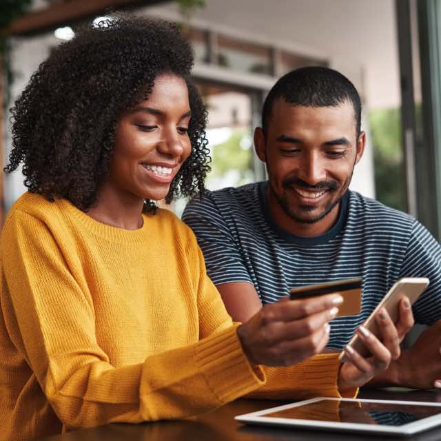 Imagem exibe mulher sorridente ao lado de um homem, segurando cartão e smartphone.
