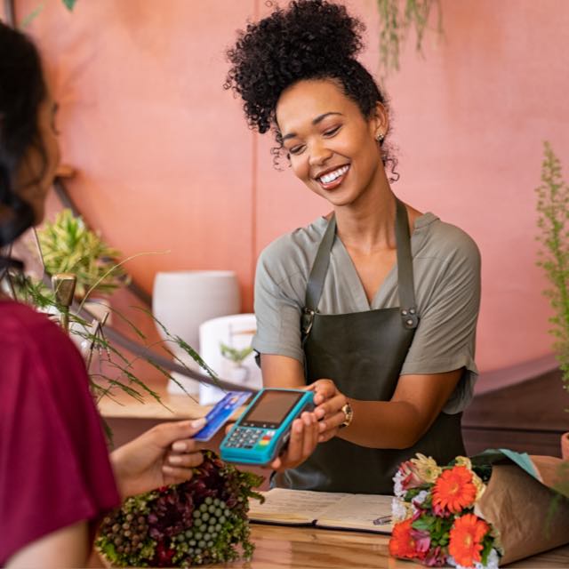 Imagem exibe uma mulher realizando pagamento por aproximação e outra mulher sorrindo segurando a maquininha